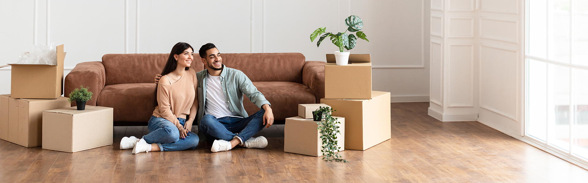 a couple sitting in a living room with plants and moving boxes